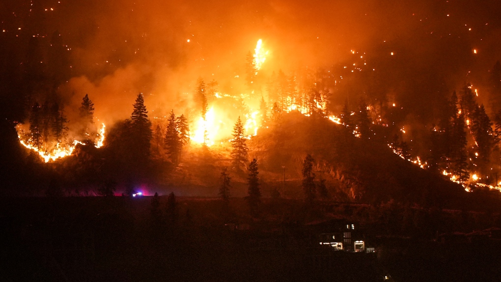 The McDougall Creek wildfire blazes along the mountainside adjacent to a lakeside residence in West Kelowna, British Columbia, on Friday, August 18, 2023